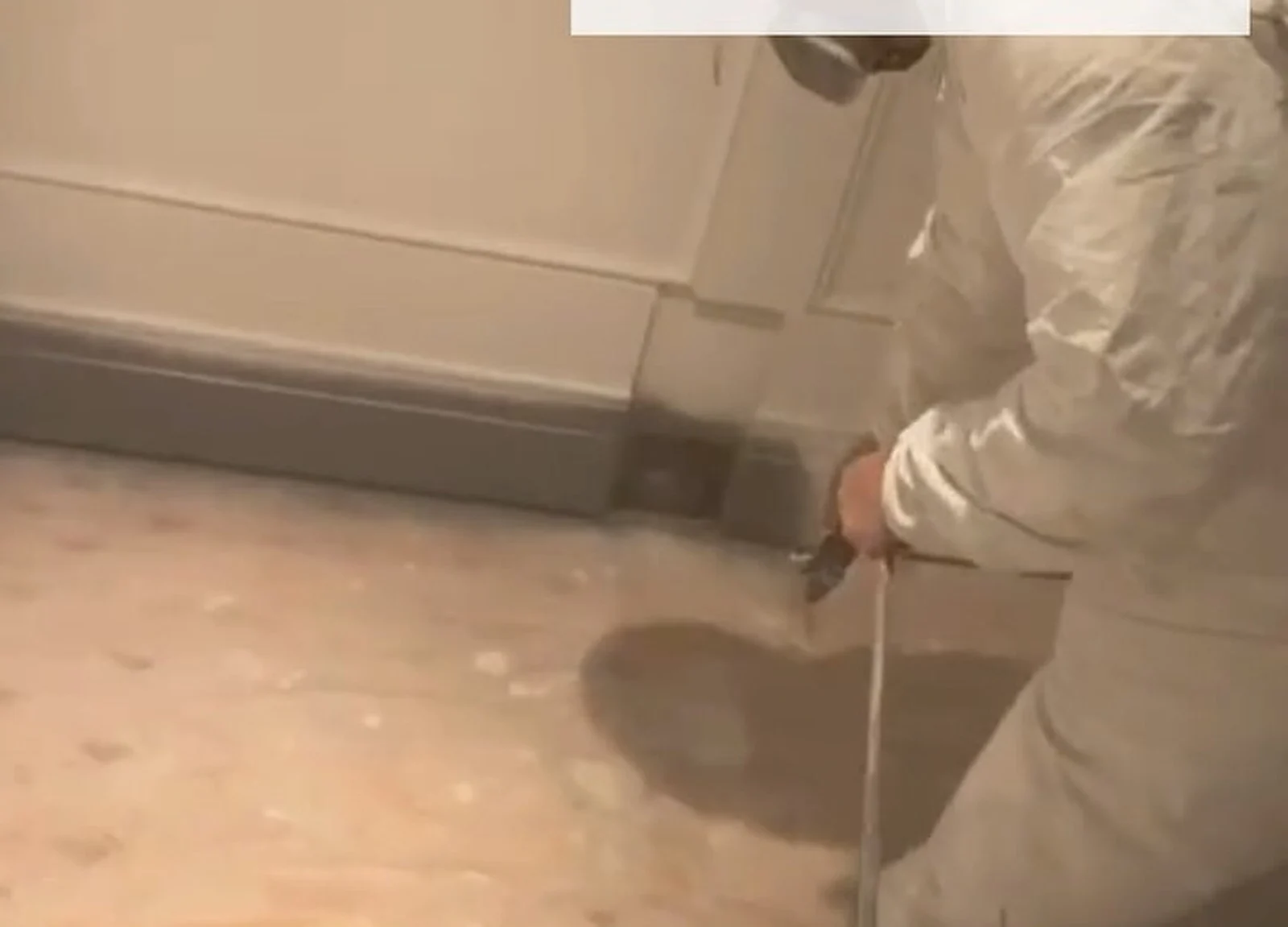 DURING: painter in white suit spraying baseboard
